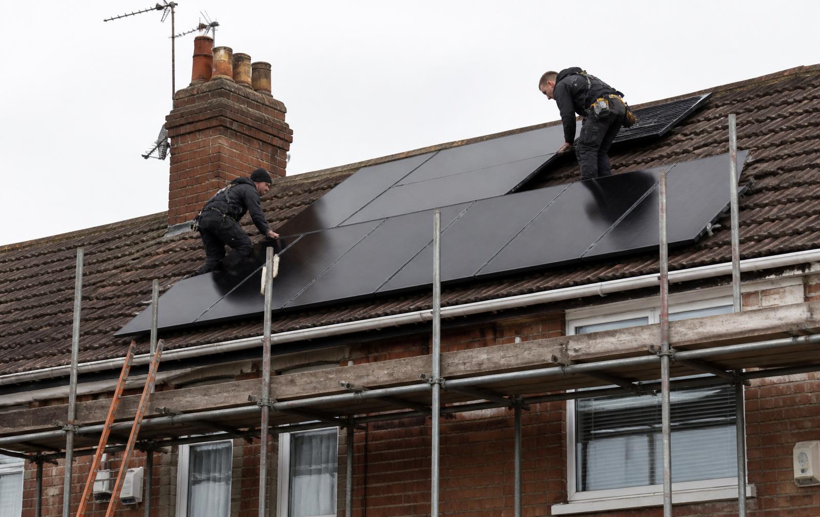 Two Wattfield installers fitting black solar panels to a brick house roof from scaffolding